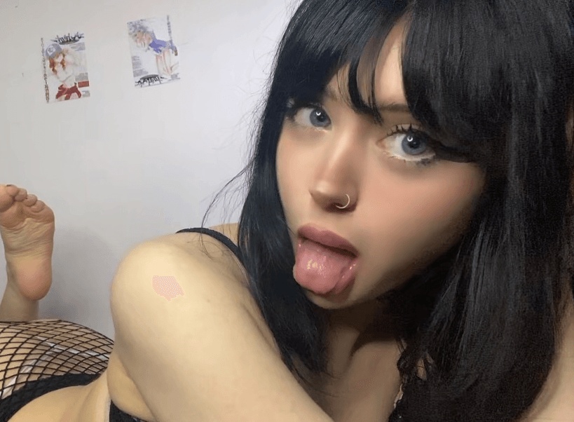 Close-up selfie of a young woman with dark hair and a nose ring sticking out her tongue while looking at the camera.