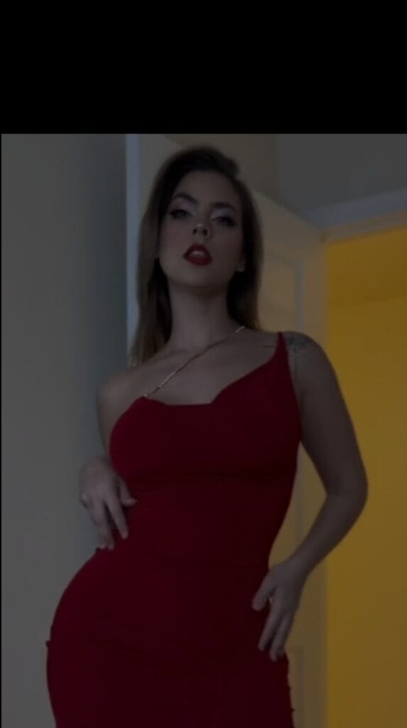 Woman in a red one-shoulder evening dress posing indoors, looking at the camera.