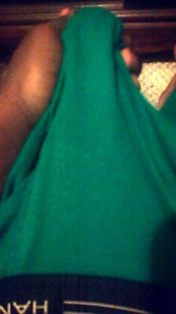 Person wrapped in bright green cloth, covering their head and face in a dim setting.