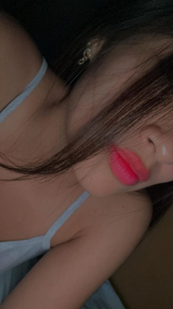 Close-up of a person wearing a light blue mask strap, showing pink lipstick and a small hoop earring at the ear.