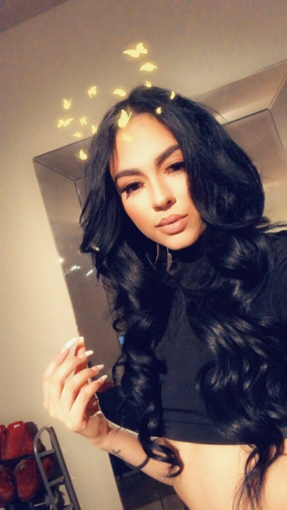 Woman with long black hair in a black top, butterfly filter above her head indoors.