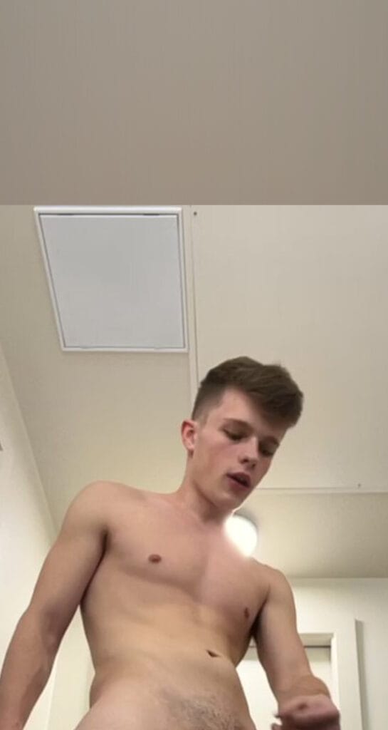 Young man standing topless in a bathroom, looking down at his torso.