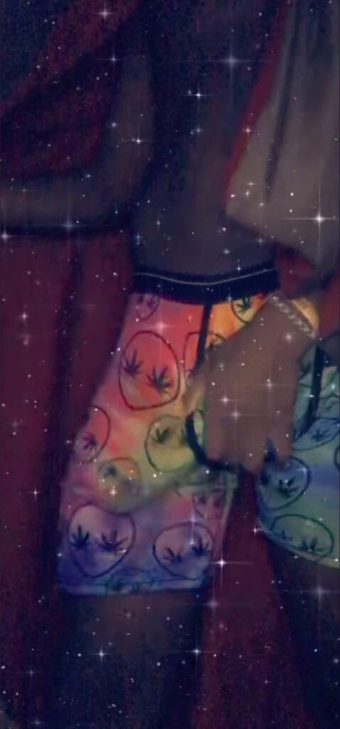 Person wearing bright shorts with circular leaf patterns, standing with a hand near the hip, a starry glitter filter over the image.