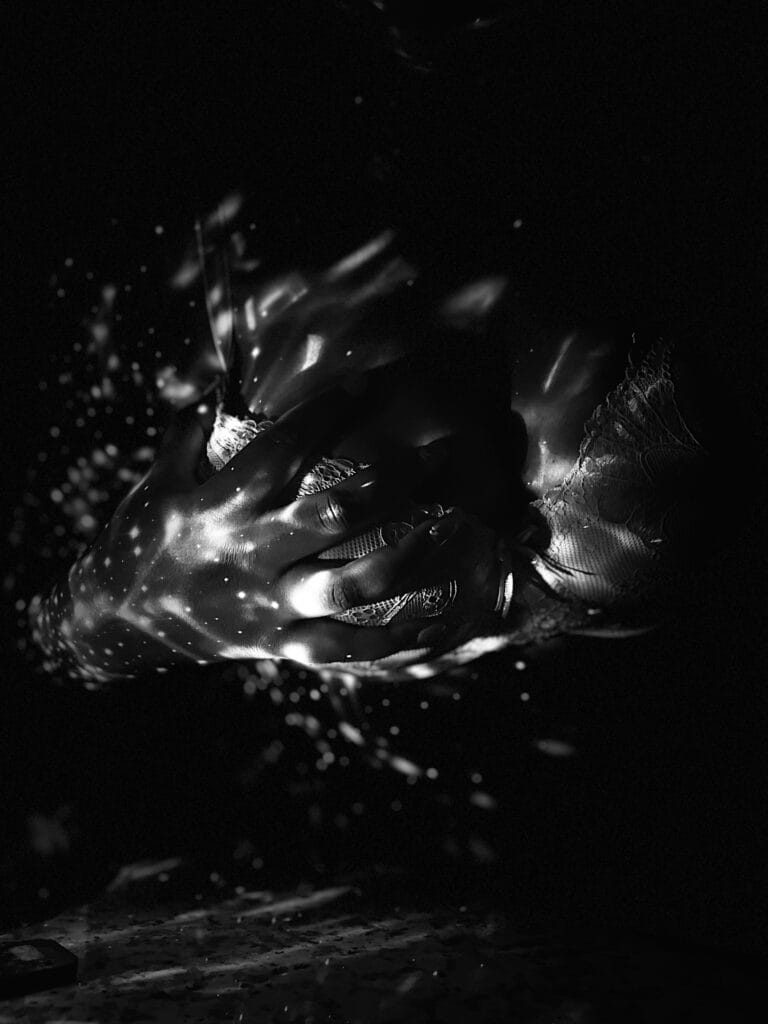 Close-up of hands clasping a lace fabric in low light, with scattered light specks around them.
