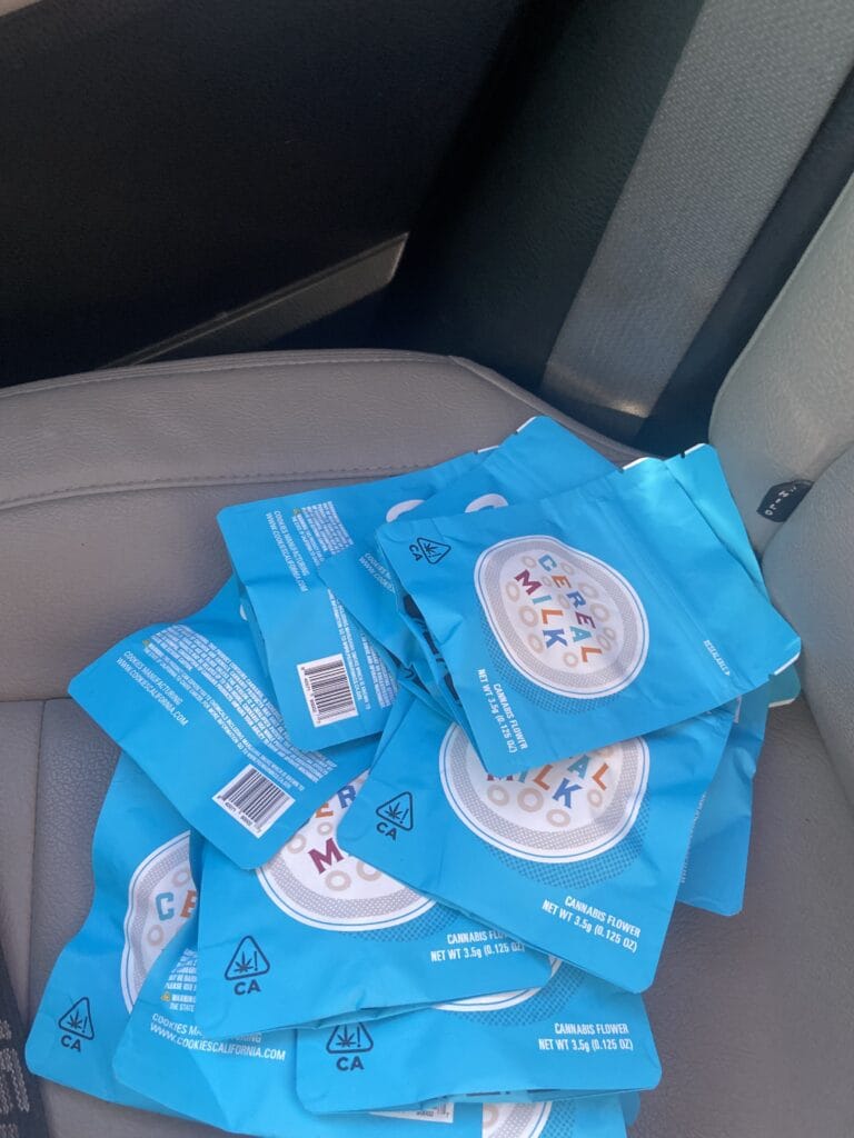 Blue cannabis-flower packaging bags scattered on a car seat, with visible CA warning symbols and text like 'Cannabis Flower'