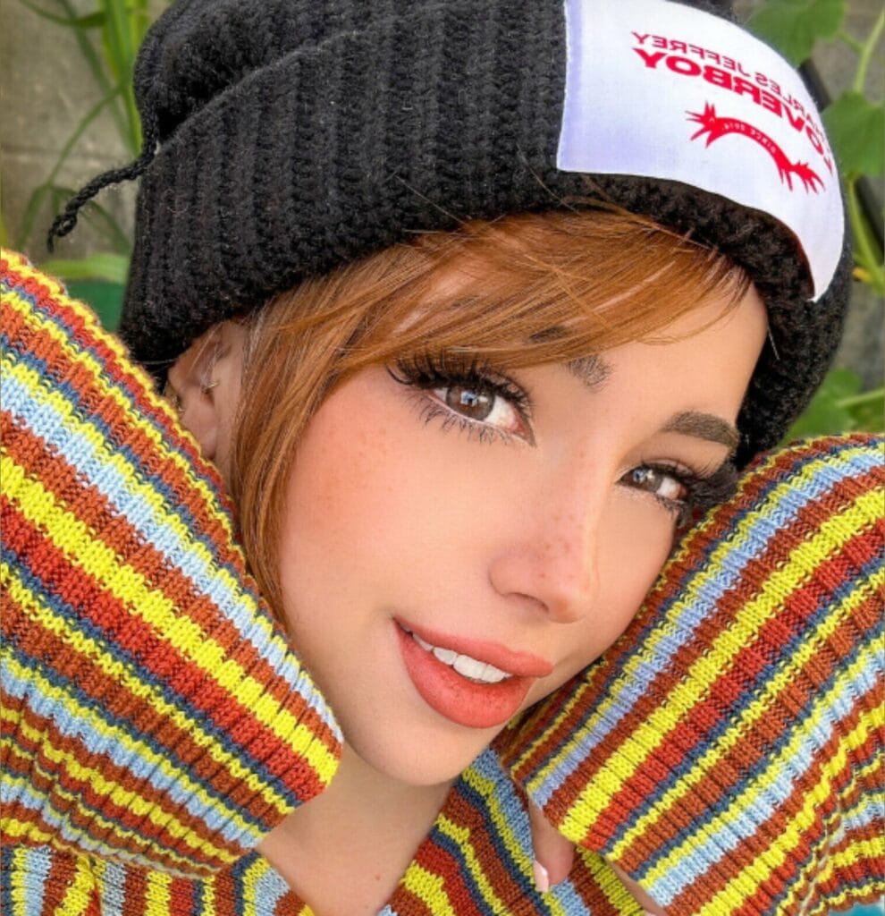 Close-up of a smiling woman in a black knit hat with a white patch, wrapped in colorful striped sleeves.