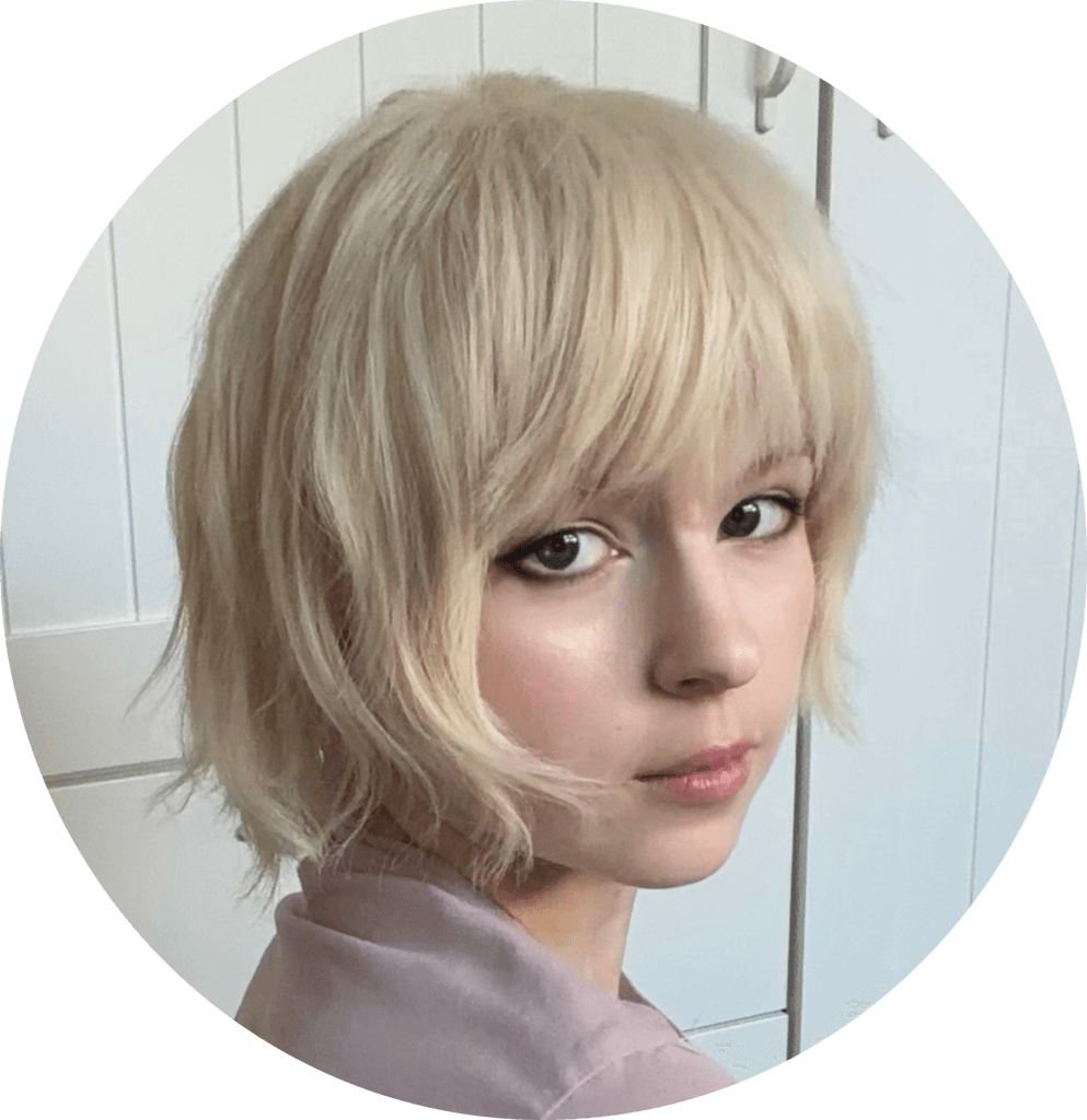Close-up of a woman with short blonde hair looking to the right, wearing a pale pink top.